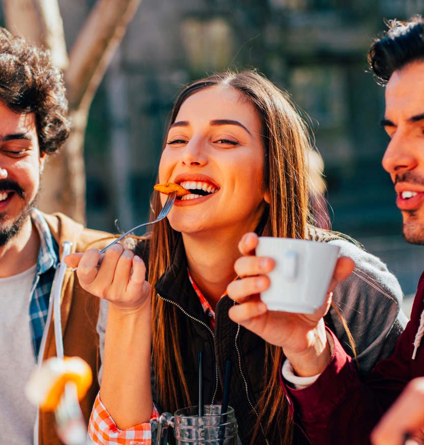 Gruppo di amici che mangiano e ridono insieme all’aperto durante un pranzo in un ristorante italiano